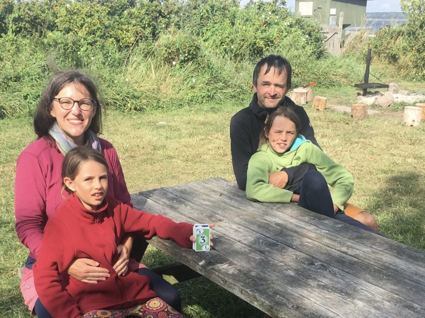 5D1B1469-8F0B-47BF-A25B-4A4564C3DE4C Familie mit zwei Kindern draußen am Tisch.